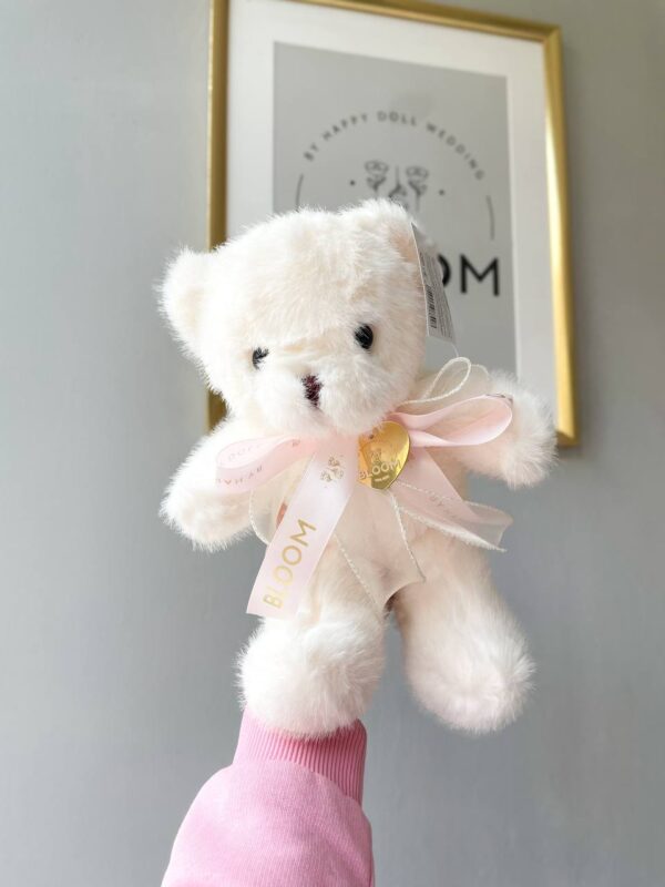 М’який кремовий плюшевий ведмедик зі стрічкою Bloom в руках.