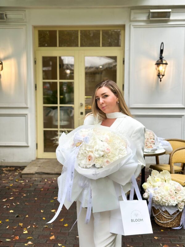 жінка з великим білим букетом із троянд, гортензії та хризантем від Bloom by Happy Doll на фоні кав’ярні