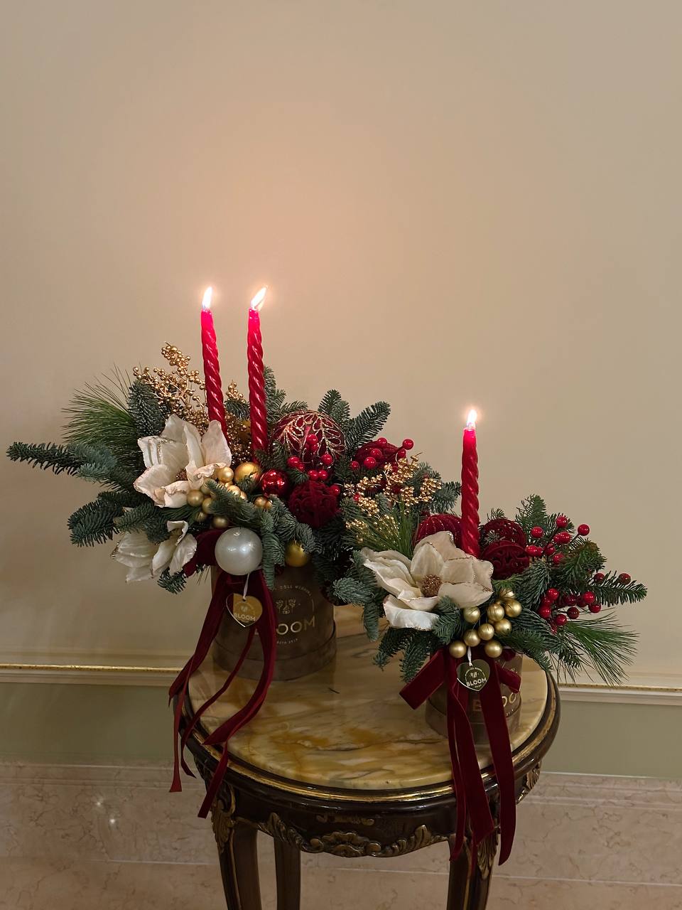 Різдвяне світло 2 Новорічні композиції у двох золотих коробках зі свічками, червоними акцентами, білими квітами та ялинковими гілками.