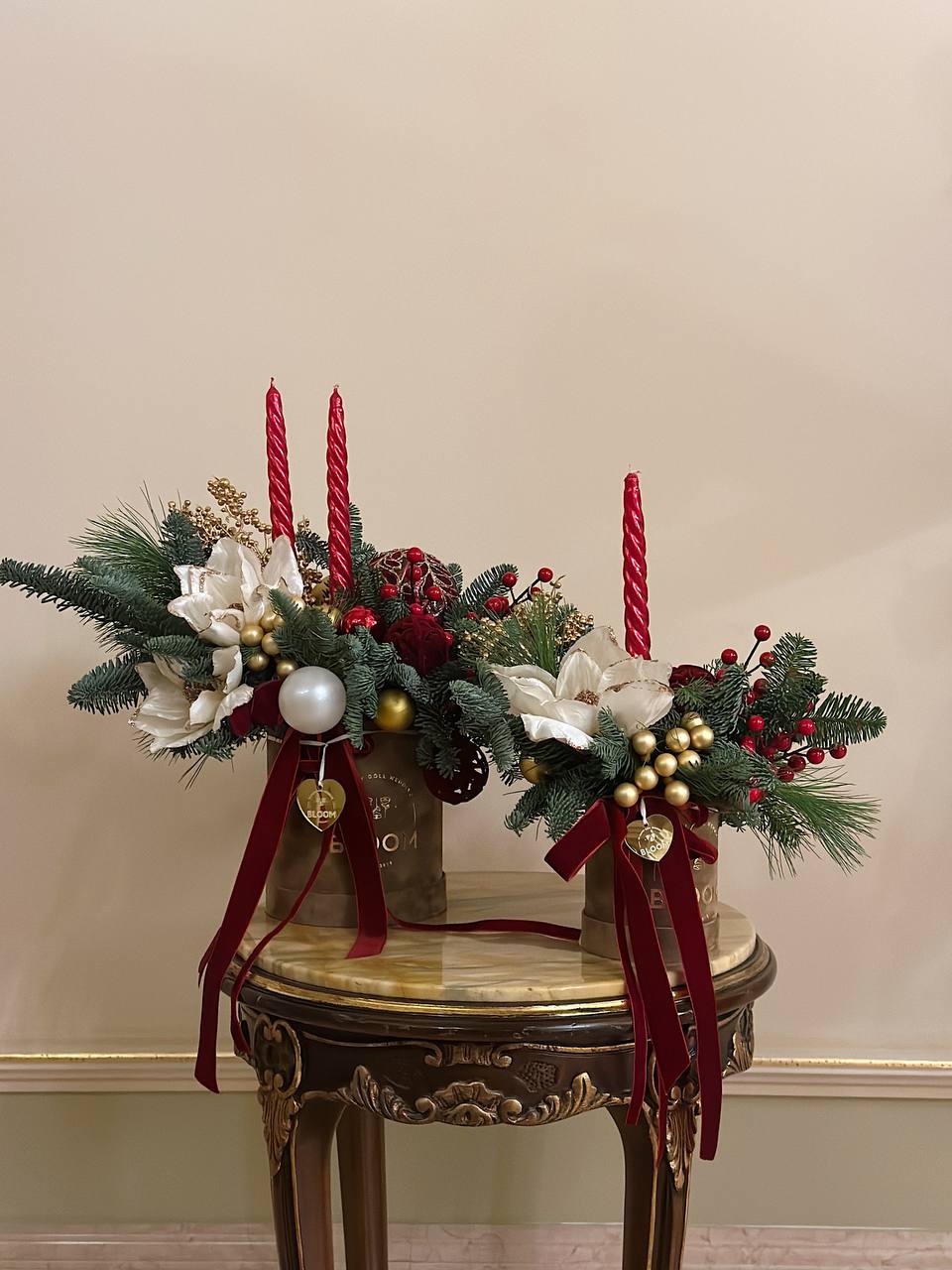 Різдвяне світло 1 Новорічні композиції у двох золотих коробках зі свічками, червоними акцентами, білими квітами та ялинковими гілками.