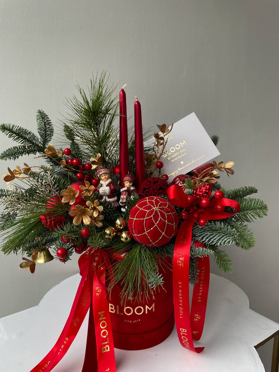 Christmas Magic in Bloom / Різдвяна магія в Bloom 3 Різдвяна композиція Bloom у червоній коробці з хвойними гілками, свічками, іграшками та святковим декором в червоно-золотій гамі.