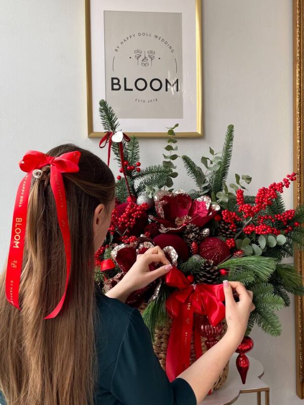 Новорічний кошик із хвоєю, червоними ягодами, декором та великим святковим бантом у червоному кольорі.