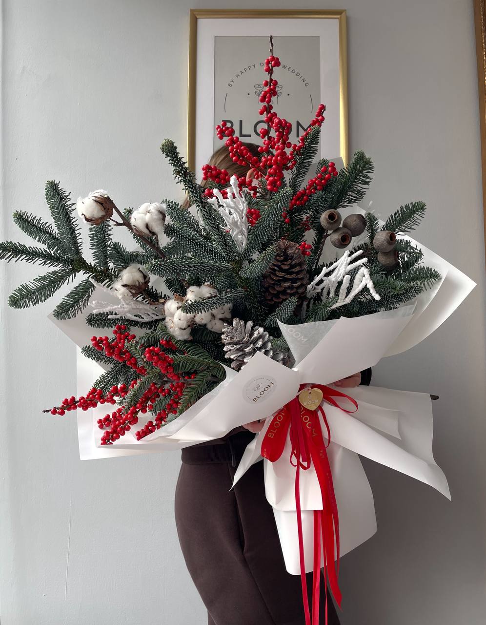 Snow elegance / Снігова елегантність 1 Зимова композиція з ялиновими гілками, білою бавовною, червоними ягодами та великими шишками, оформлена у білий папір із червоними стрічками.
