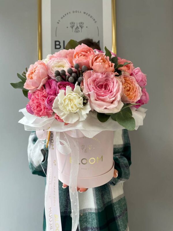 Авторська композиція в рожевій коробці Bloom із садовими трояндами, ранункулусами, півоніями та діантусами у ніжно-рожевих тонах.