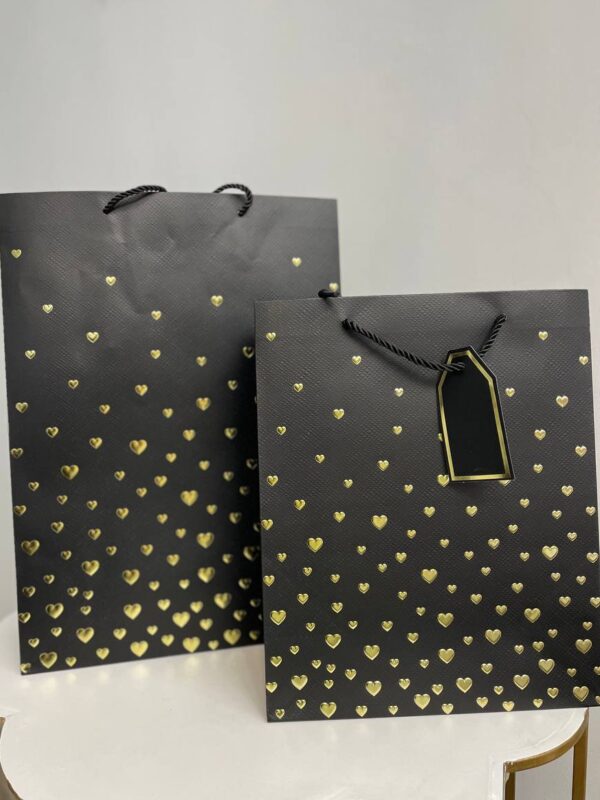 Чорний паперовий подарунковий пакет із золотими сердечками та подарунковою біркою