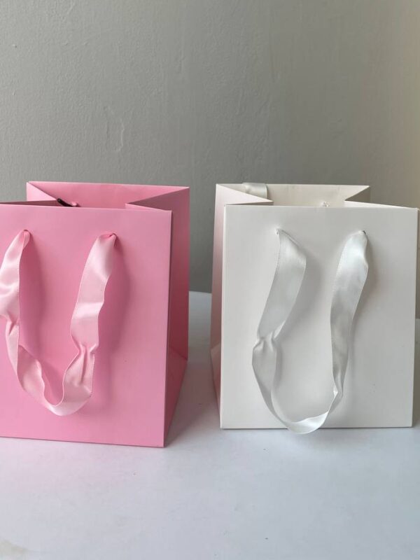 Однотонні паперові подарункові пакети рожевого та білого кольору з атласними ручками