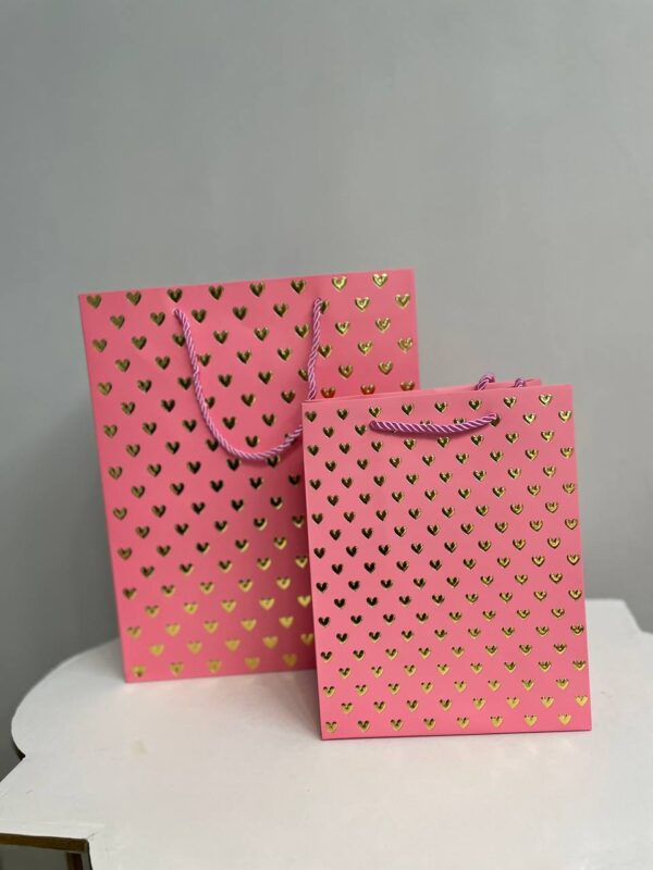 Рожевий паперовий подарунковий пакет із золотими сердечками та крученими ручками