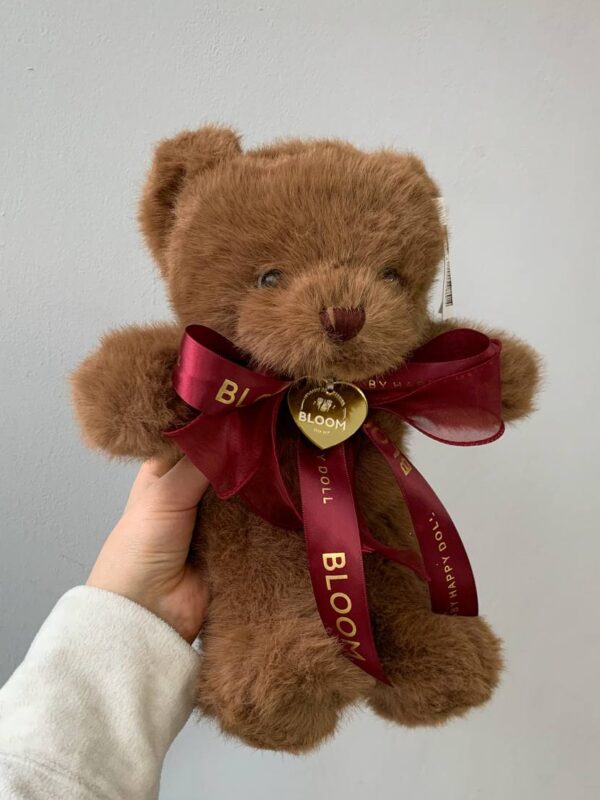 Плюшевий коричневий ведмедик Bloom з бордовою фірмовою стрічкою в руці