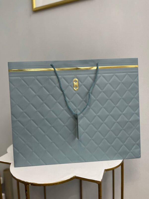 Світло-сірий паперовий подарунковий пакет з ромбоподібним тисненням, золотими акцентами та крученими ручками