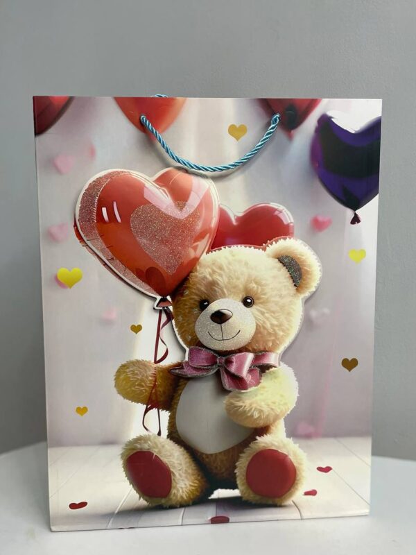 Паперовий подарунковий пакет з ведмедиком, який тримає повітряне серце, з блакитними ручками