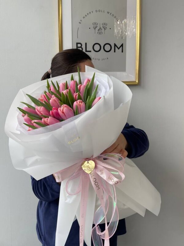 Букет з рожевих тюльпанів у білій упаковці Bloom з рожевими декоративними стрічками.