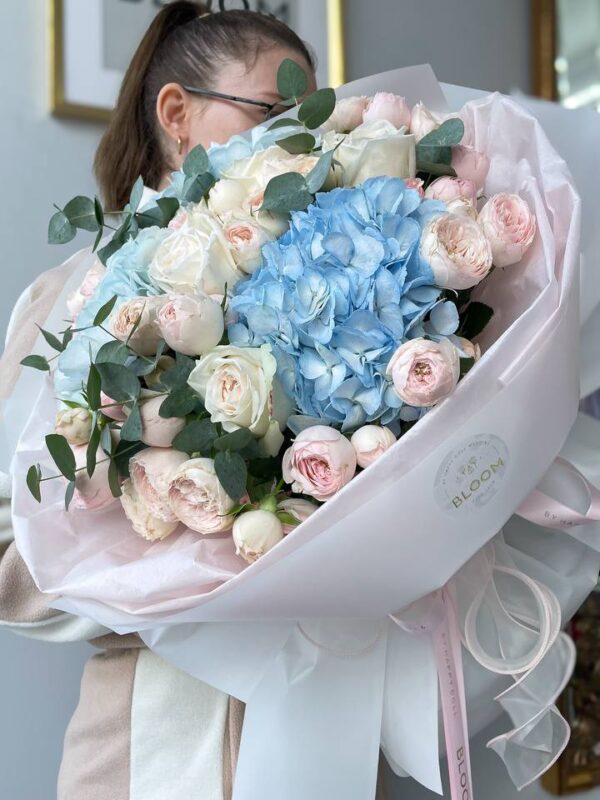 Ніжний букет квітів з блакитною гортензією, кремовими та рожевими трояндами і евкаліптом у білій упаковці Bloom.
