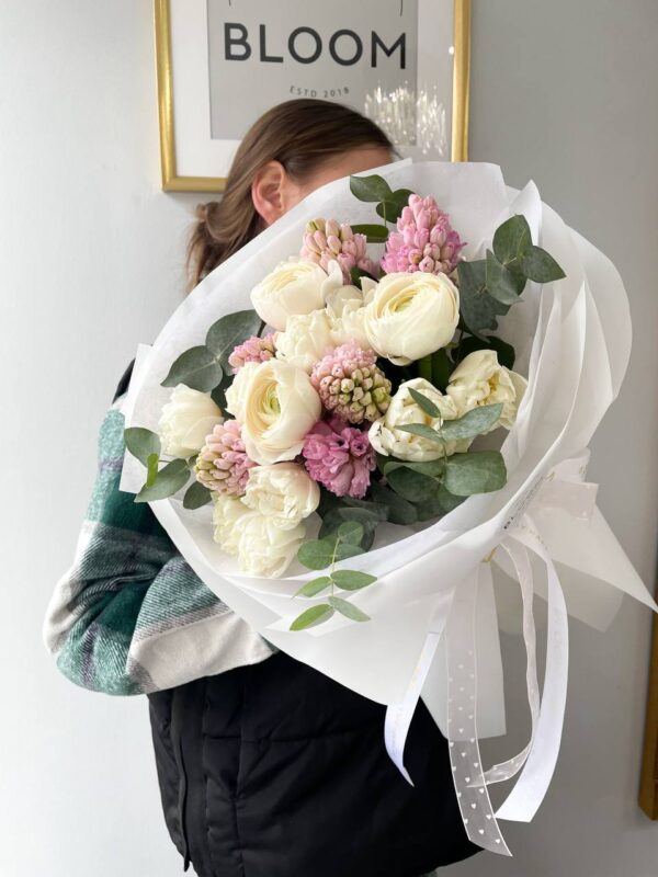 Ніжний букет квітів з білими ранункулюсами, рожевими гіацинтами та евкаліптом у білій упаковці Bloom.