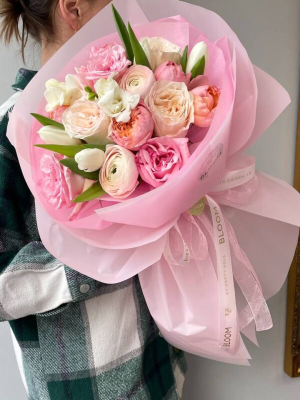 Букет у рожево-кремових тонах з ранункулюсами, трояндами та тюльпанами у рожевій упаковці Bloom.