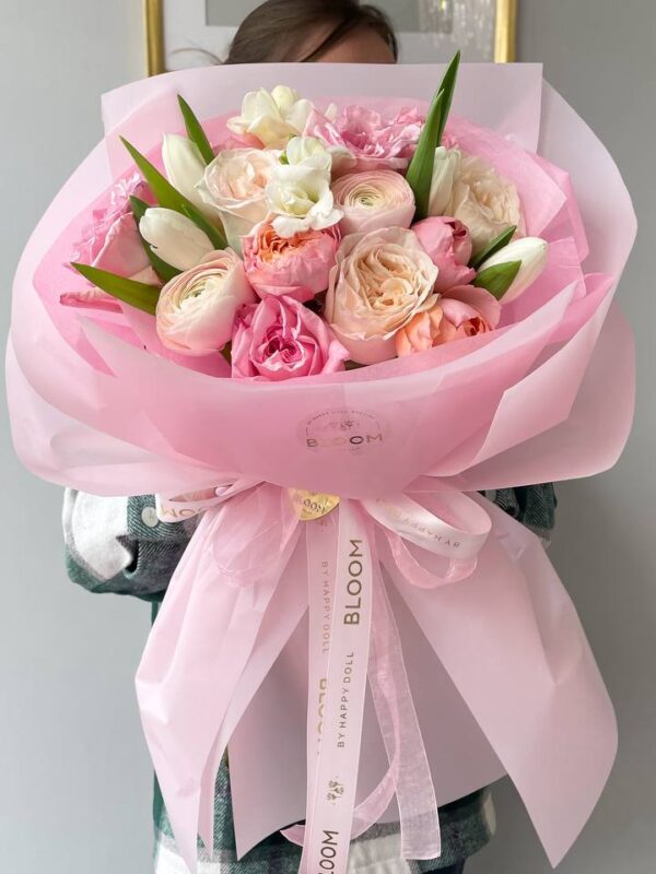 Букет у рожево-кремових тонах з ранункулюсами, трояндами та тюльпанами у рожевій упаковці Bloom.