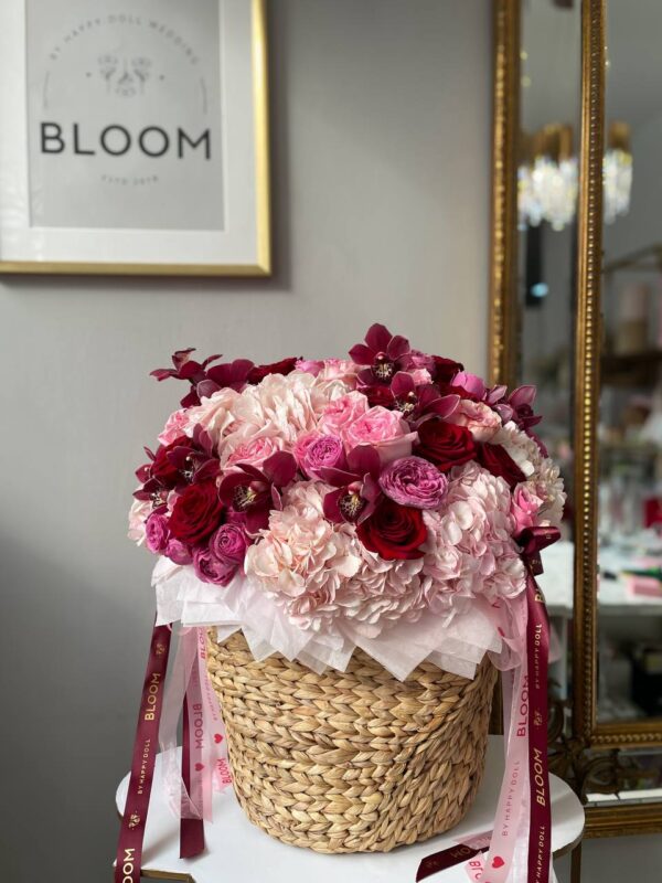 Розкішна квіткова композиція у плетеному кошику з рожевою гортензією, червоними трояндами та орхідеями Bloom.