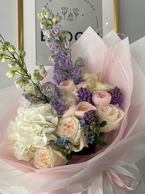 Букет з білою гортензією, кремовими трояндами та лавандовим дельфініумом у ніжній упаковці Bloom.