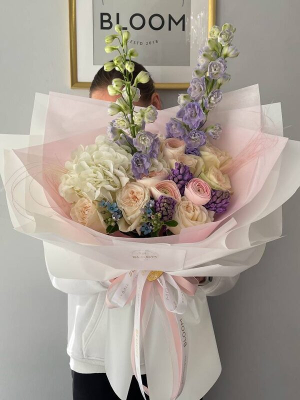 Букет з білою гортензією, кремовими трояндами та лавандовим дельфініумом у ніжній упаковці Bloom.