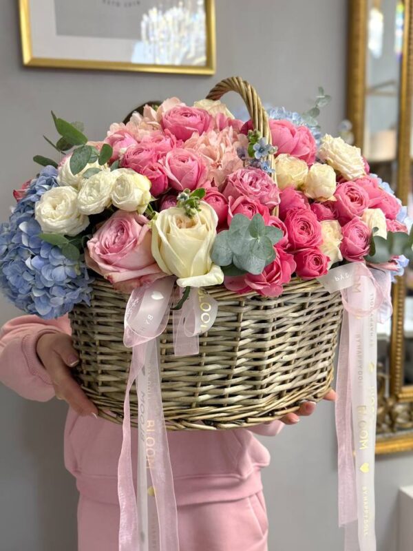 Велика квіткова композиція у плетеному кошику з рожевими трояндами, кремовими квітами та блакитною гортензією Bloom.