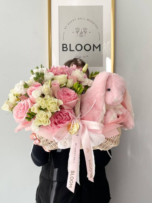 Квіткова композиція у білій корзині з рожевими та білими квітами і м’яким рожевим зайчиком від Bloom.