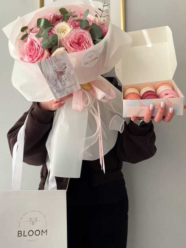Букет з рожевих троянд O’Hara, білого ранункулюса та евкаліпта поруч із коробкою макаронів від Bloom.